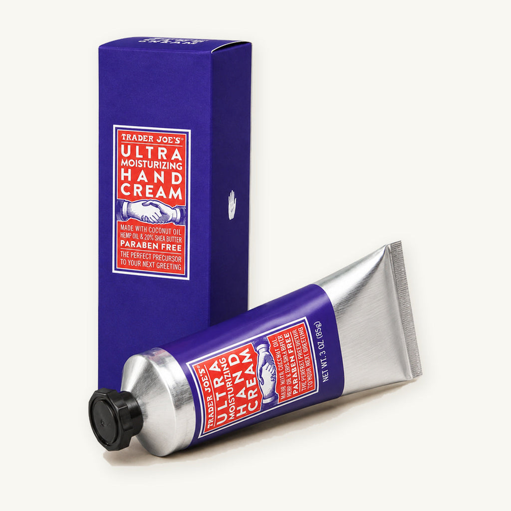 Trader Joe's Ultra Moisturizing Hand Cream, 3 oz. Silver hand cream tube beside a purple box on a warm ivory background.